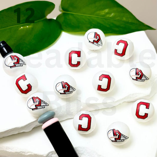 Set of white lip balm tubes with red and black designs on a white surface with green leaves in the background.

