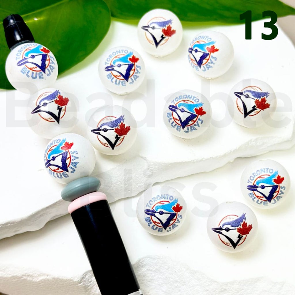 Set of Toronto Blue Jays-themed lip balms on a white surface with a green leaf in the background.


