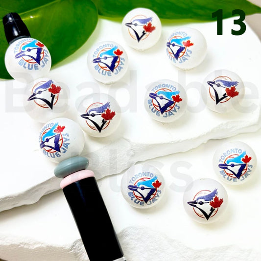 Set of Toronto Blue Jays-themed lip balms on a white surface with a green leaf in the background.

