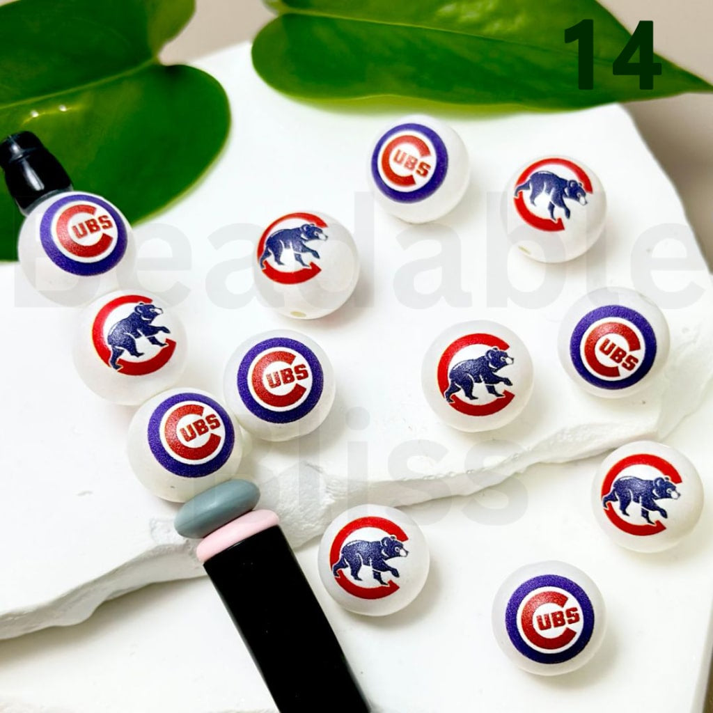 Set of Chicago Cubs-themed lip balms on a white surface with green leaves in the background.

