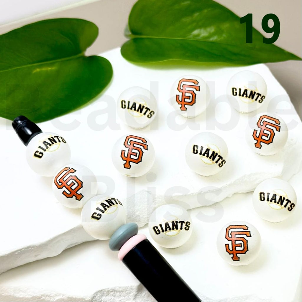 Bracelet with San Francisco Giants logo beads on a white surface with green leaves in the background.

