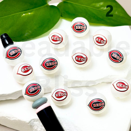 White lip balms with 'REDS' logo on a white surface with green leaves in the background.

