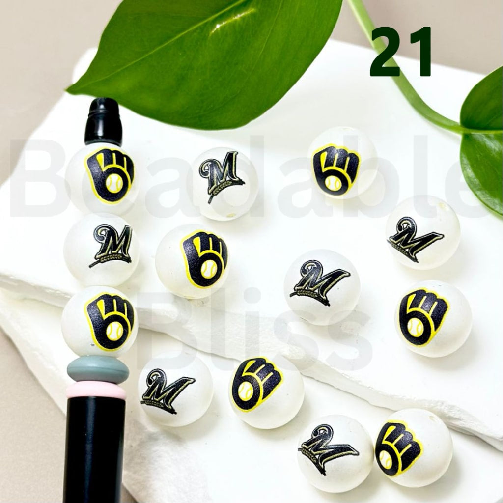 White beads with black and yellow designs on a white surface with green leaves in the background.

