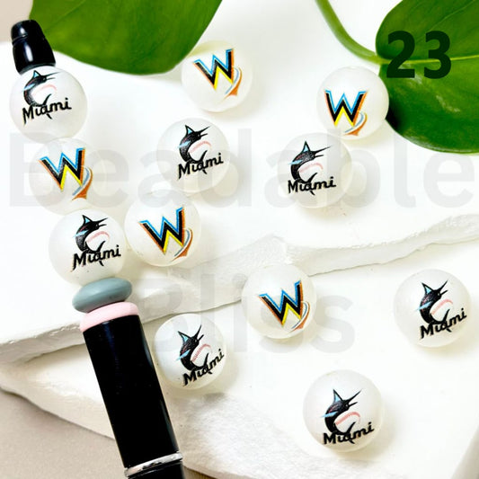 White buttons with 'W' and 'Miami' branding on a white surface with green leaves.


