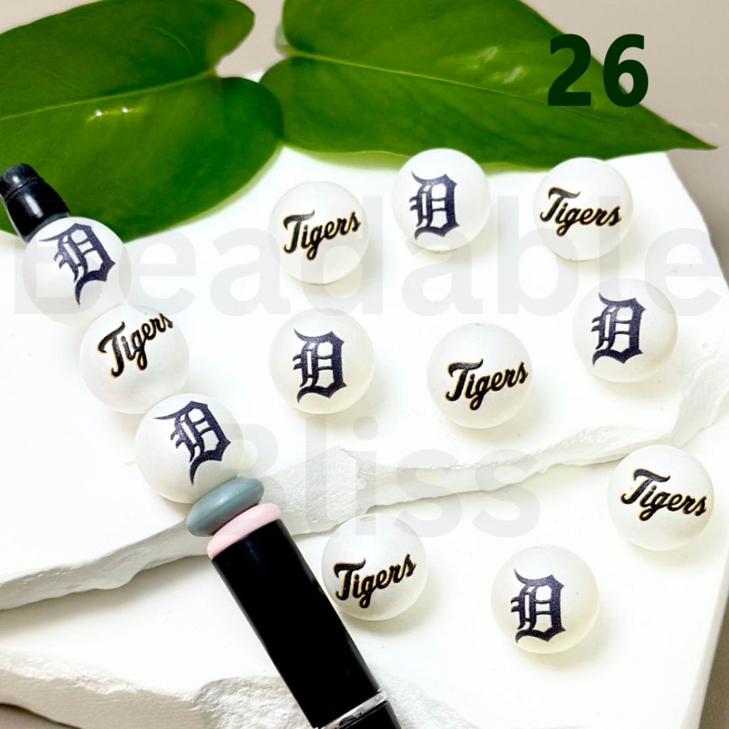 White beads with 'Tigers' and logo on a white surface with green leaves in the background

