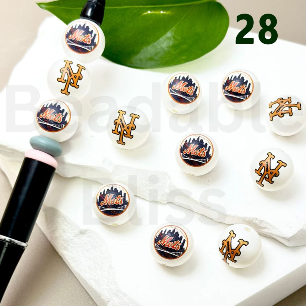 Collection of earrings with Mets logo on a white surface with green leaves in the background.

