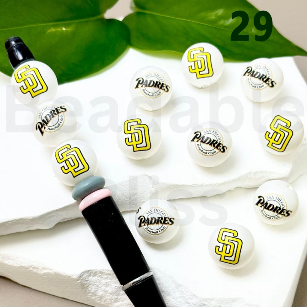 Set of San Diego Padres-themed lip balms on a white surface with green leaves in the background.

