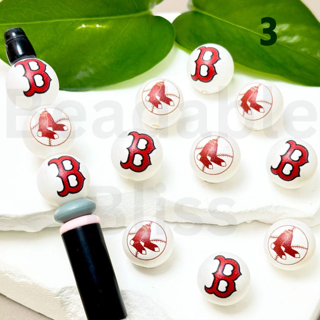 Set of white buttons with red 'B' logo on a white surface with green leaves in the background.


