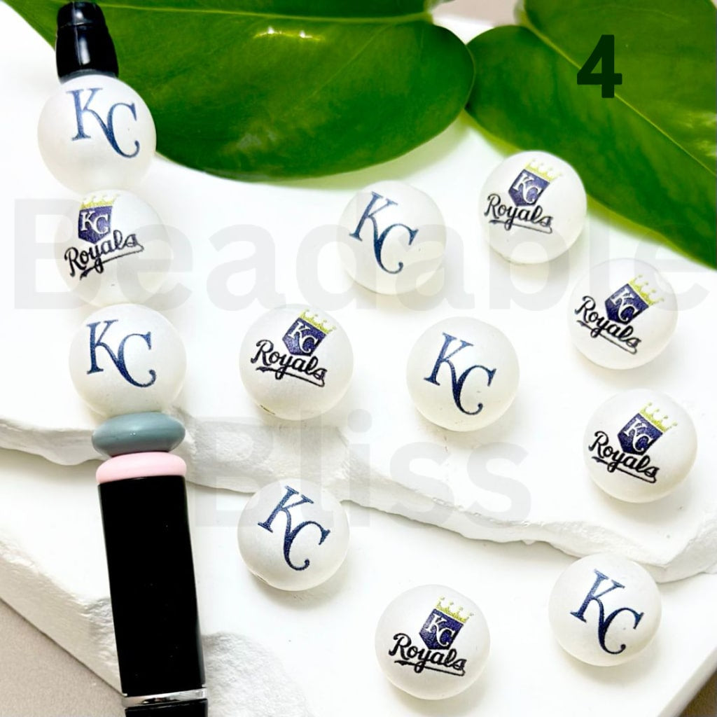 White buttons with 'KC Royals' logo on a white surface with green leaves in the background.

