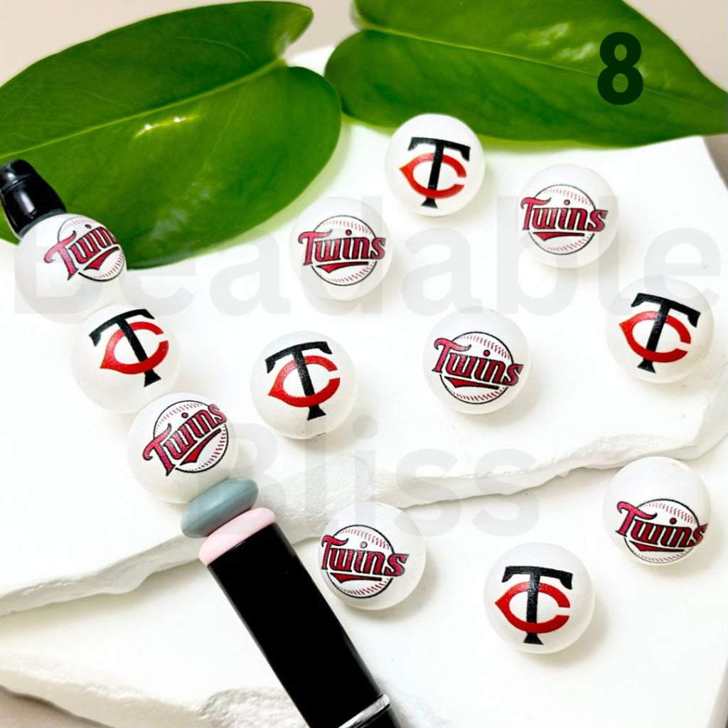 Set of Minnesota Twins-themed lip balms on a white surface with green leaves in the background.

