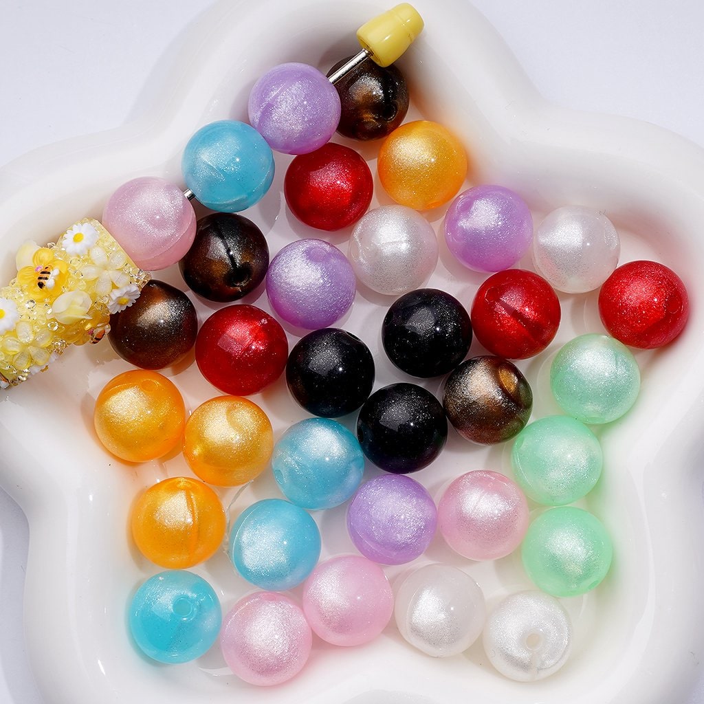 A collection of round acrylic beads in various colors including clear, red, blue, yellow, pink, purple, black, and silver, with a sparkling glitter finish.


