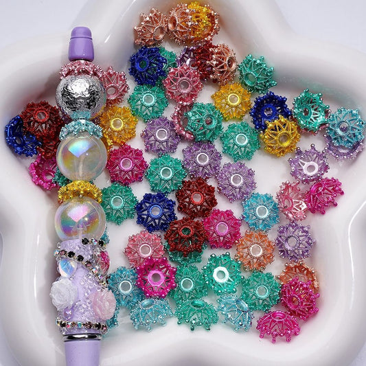 A collection of multicolored acrylic crown bead caps displayed in a petri dish, with some beads caps arranged on a pen for scale.

