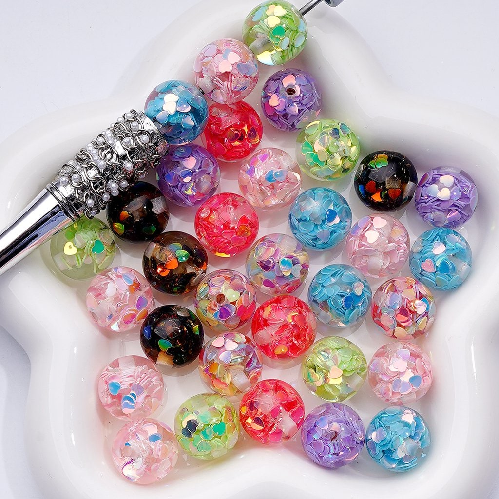Colorful glittery beads with a decorative tool on a white background

