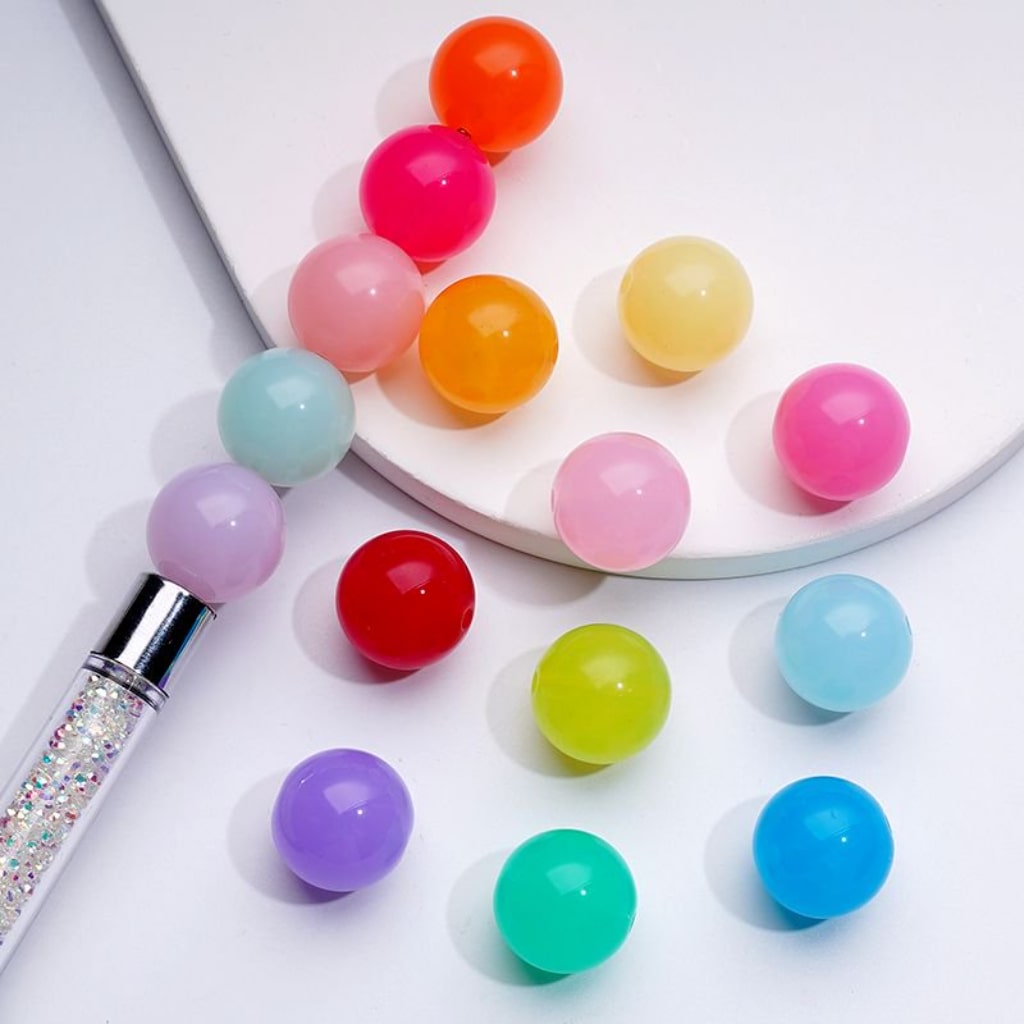 A collection of colorful glossy jelly round acrylic beads in various colors including red, orange, yellow, pink, purple, blue, and green, with a beadable pen on a white surface.

