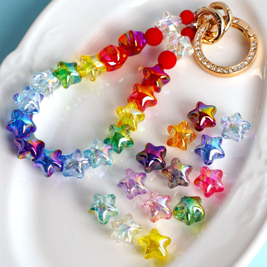 A collection of multicolored translucent acrylic beads shaped like five-pointed stars, displayed on a white surface.

