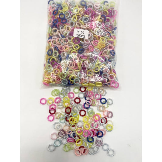 A clear plastic bag containing multicolored pearl acrylic spacers, with a few spacers scattered outside the bag on a white surface.


