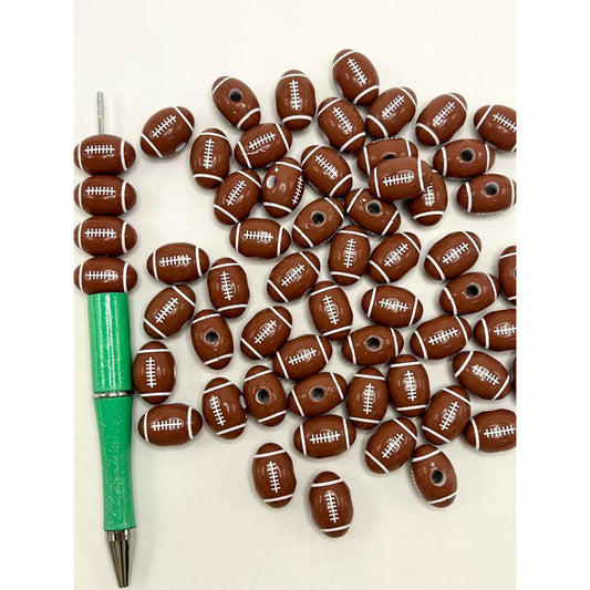 Acrylic beads designed to look like brown American footballs with white stripes, arranged on a white surface next to a green bead pen.


