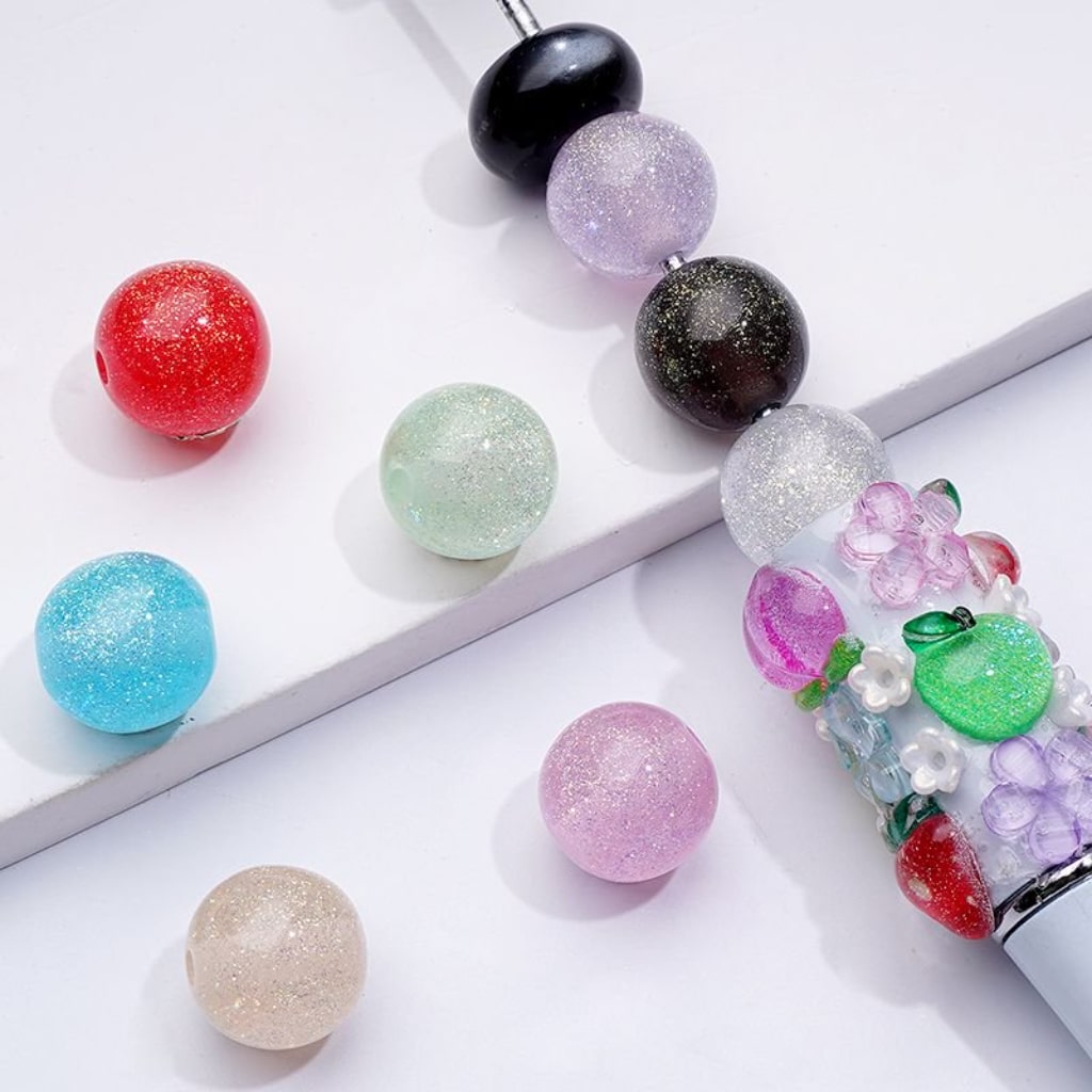 A collection of colorful round acrylic beads in glittery finish, displayed in various colors including red, blue, green, purple, beige, black, and clear.

