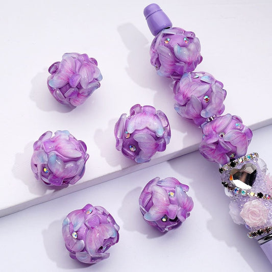 A collection of purple fish tail clay beads with AB rhinestones, approximately 20mm in size, displayed on a surface.

