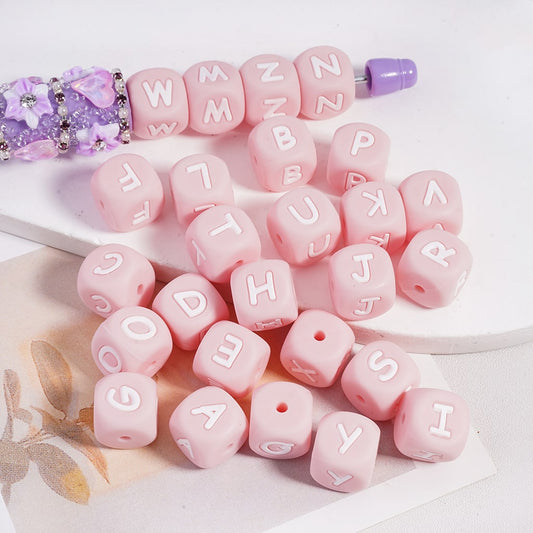 Pink letter beads with a purple and white bead on a white surface