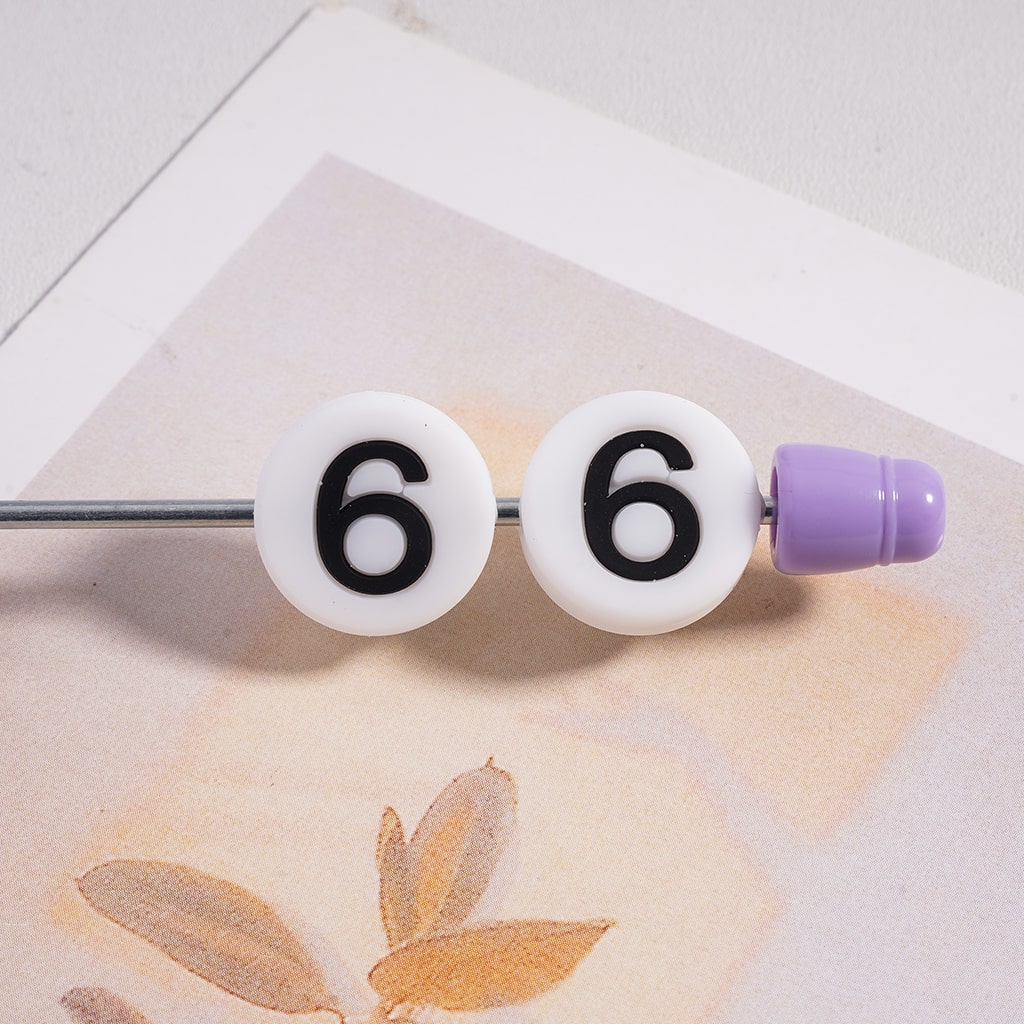 Beaded hair stick with number '6' on a textured surface