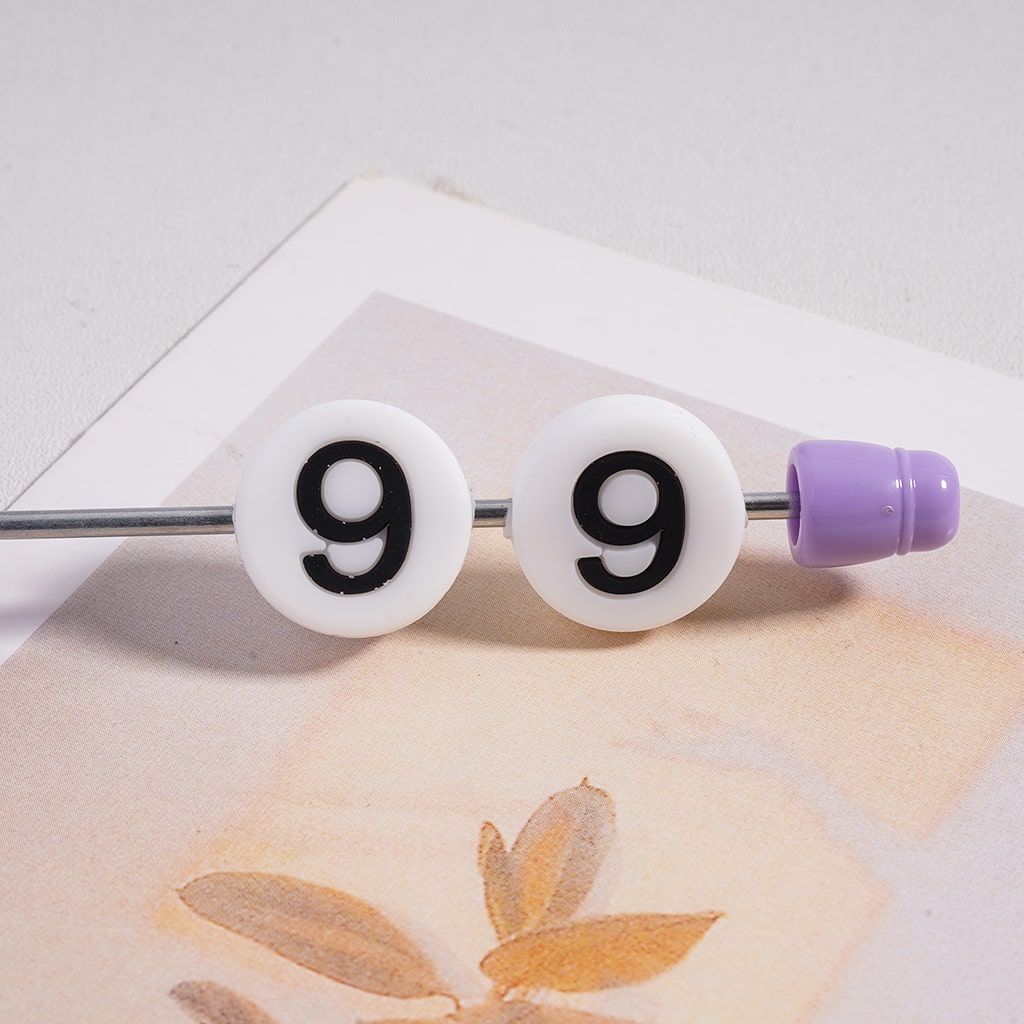 Two white beads with black '9' numbers on a metal rod with purple end cap, placed on a textured surface.