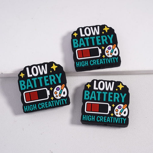 Three 'Low Battery High Creativity' pins on a white background