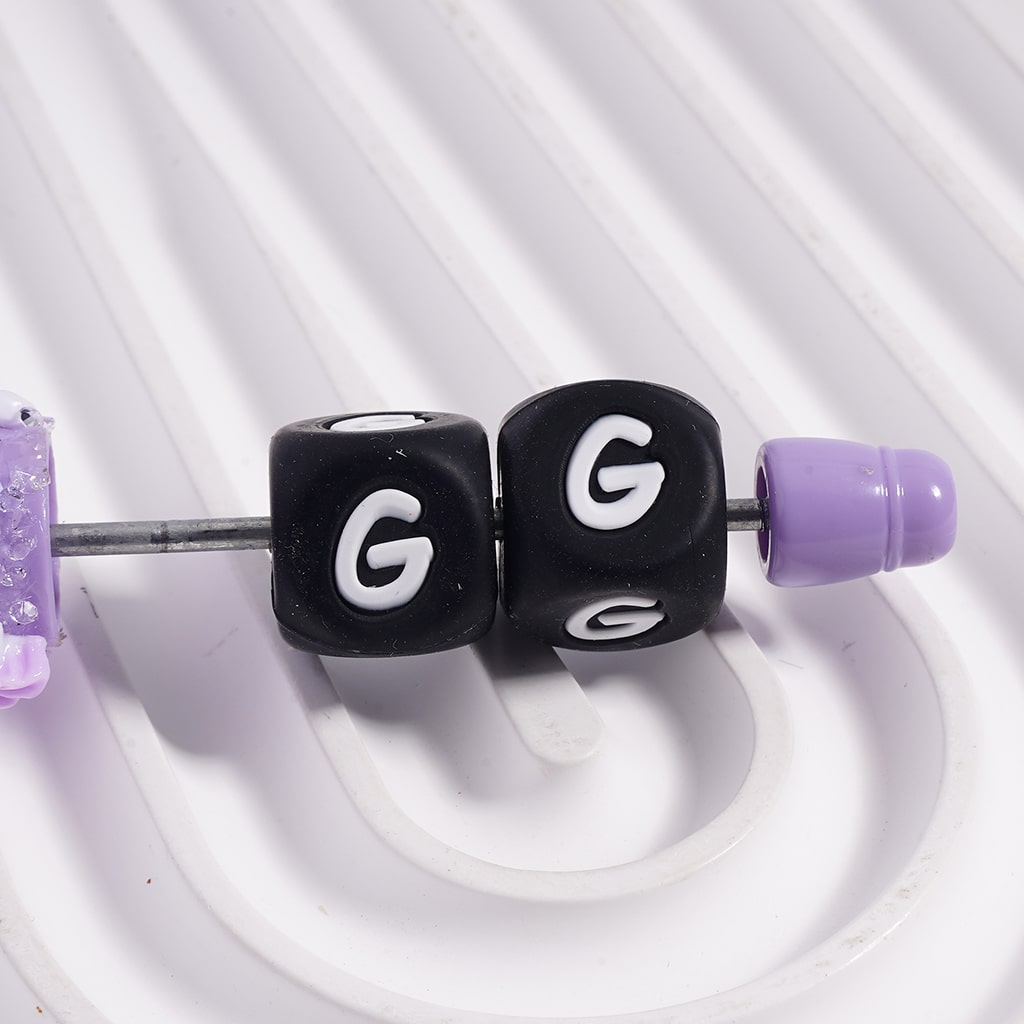 Black beads with 'G' lettering on a white background