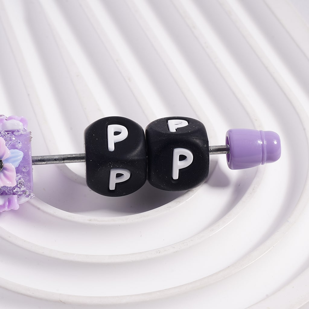 Belly button ring with black beads labeled 'P' and purple accents on a white background