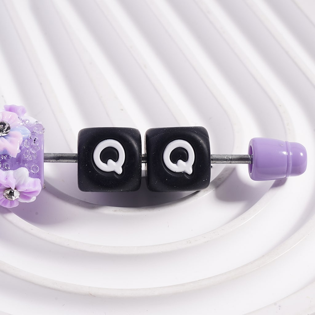 Jewelry with black beads featuring white letters 'Q' on a white background