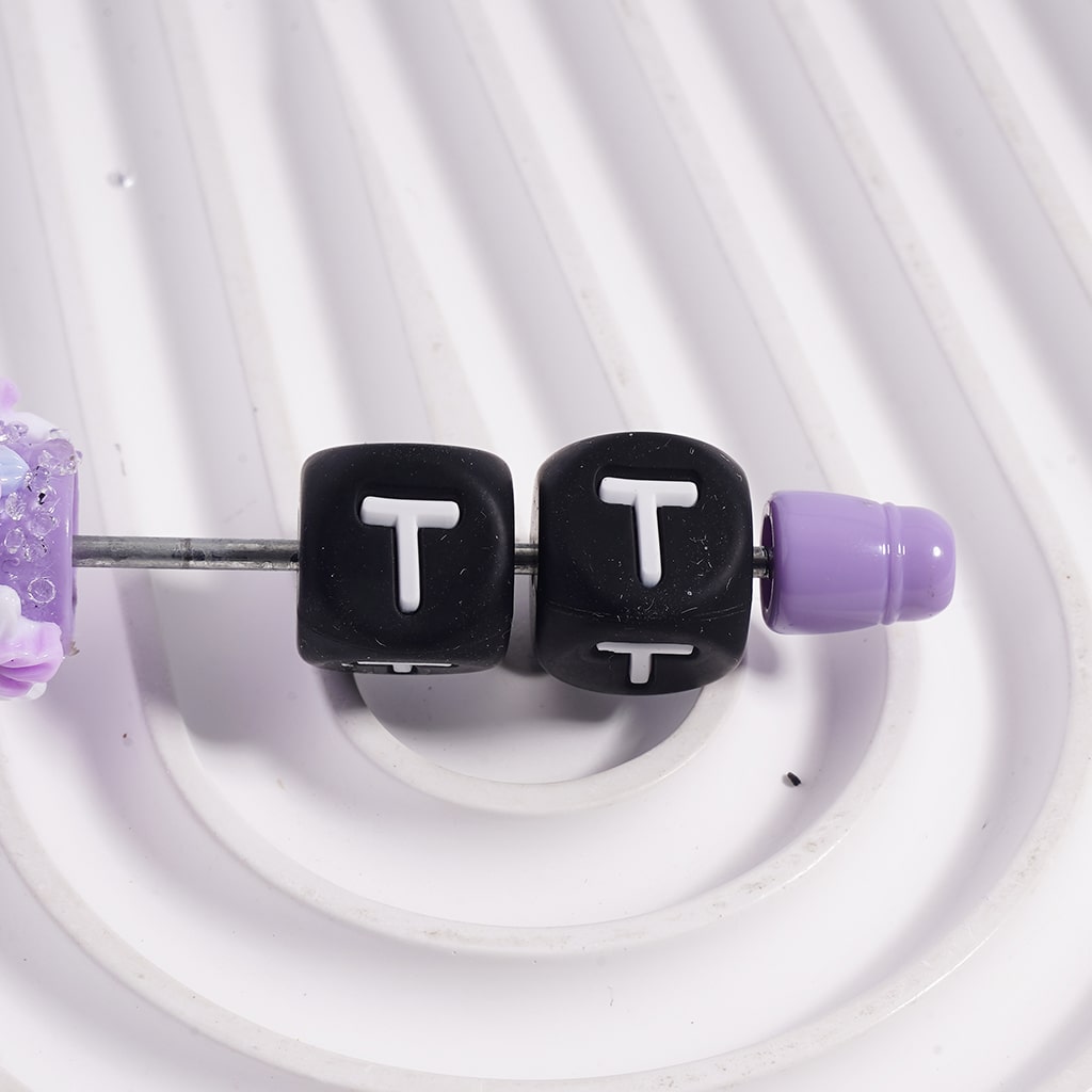 Black cube-shaped earrings with 'T' letters and purple accents on a white background