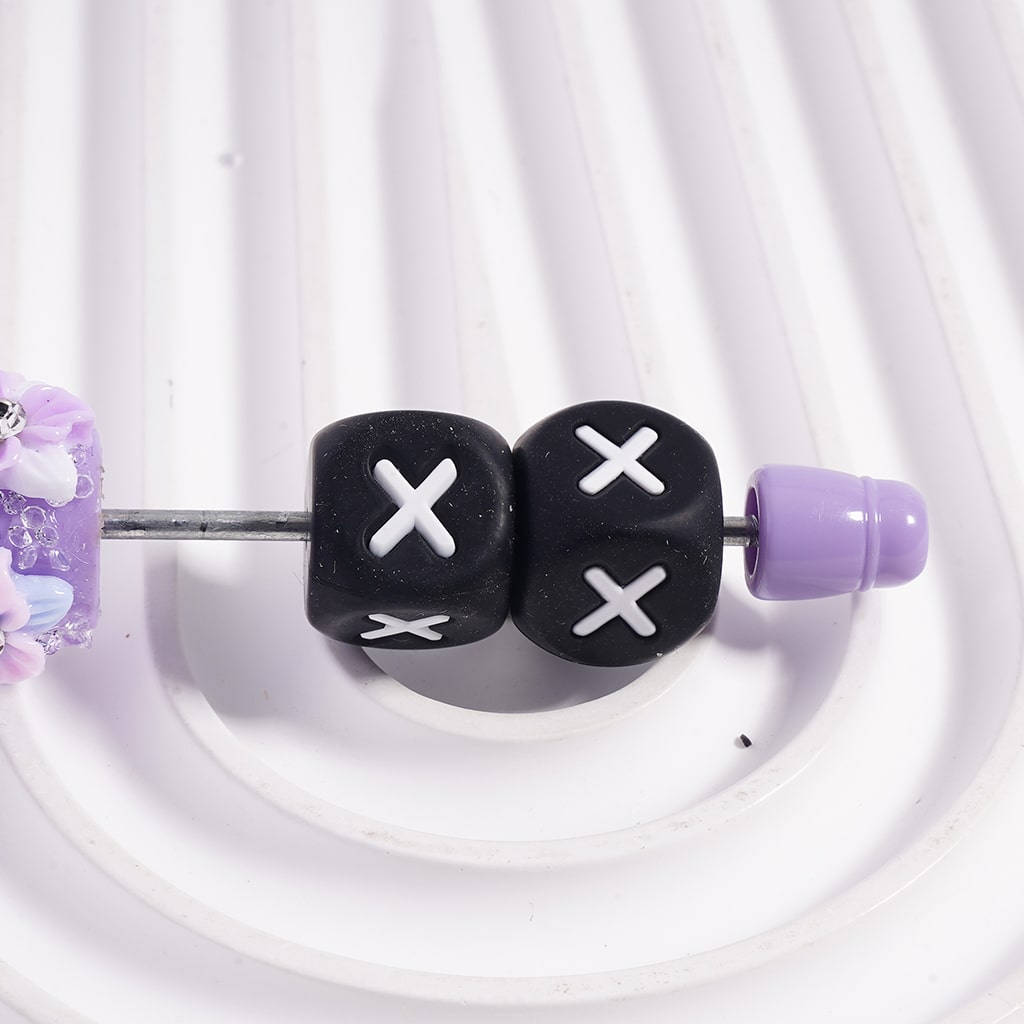 Black dice-shaped beads with white crosses on a white background