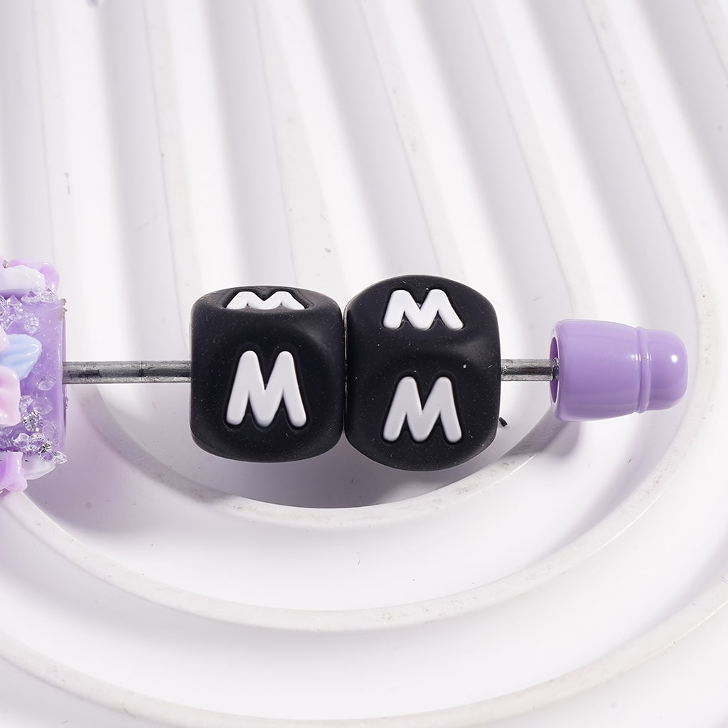 Black beads with 'M' lettering on a white background