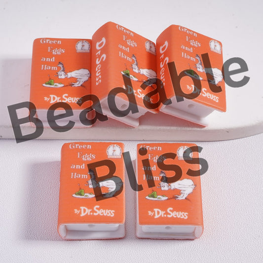 Open book of 'Green Eggs and Ham' by Dr. Seuss with two closed copies on a white background.