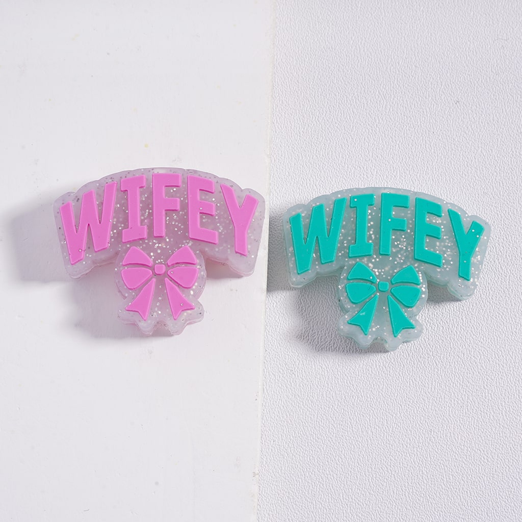 Two 'WIFEY' earrings with pink and green text on a white background