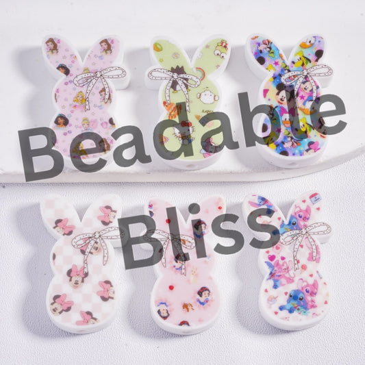 Colorful bunny-shaped beads with cartoon characters on a white plate, branded 'Beadable Bliss'.