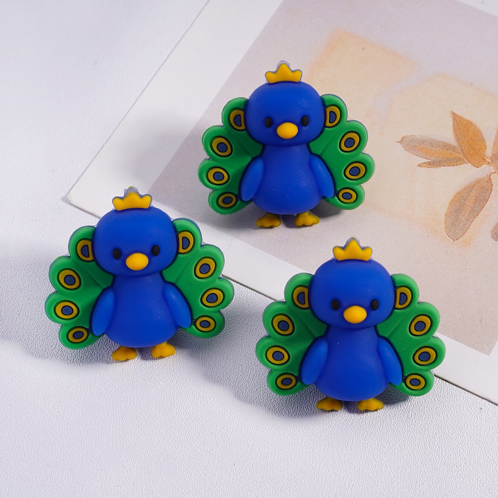 Three blue peacock-shaped earrings on a white surface with a floral background.