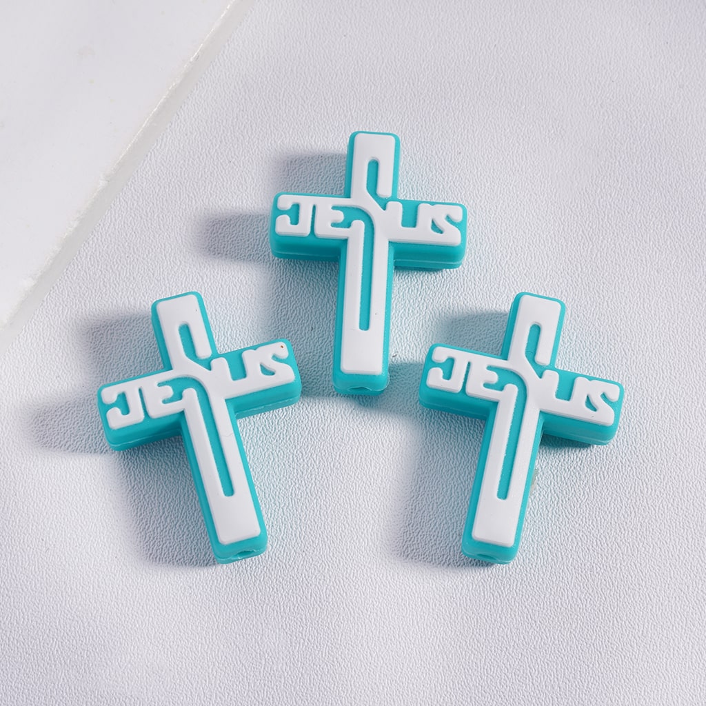 Three turquoise and white cross-shaped 'Jesus' charms on a light gray background