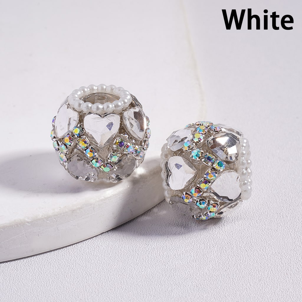 Two decorative beads with heart designs and multicolored stones on a white surface.
