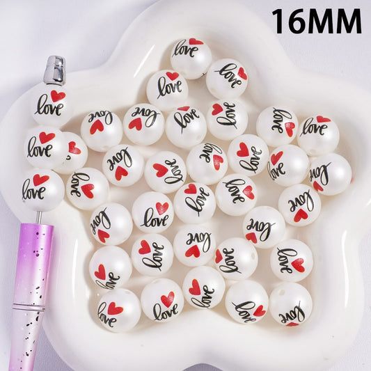 White beads with 'Love' and heart designs on a white dish with a pink pen.