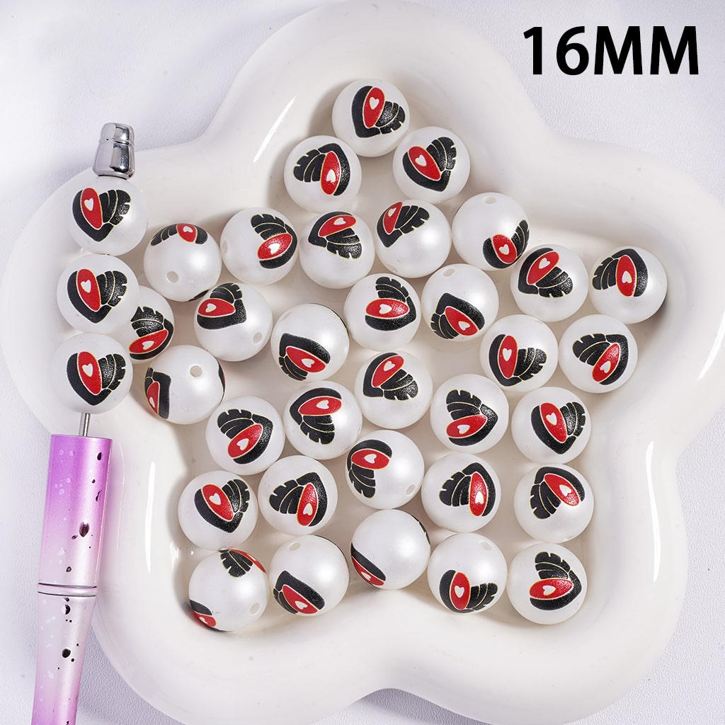 White beads with red and black designs on a white dish, with a pen for scale.