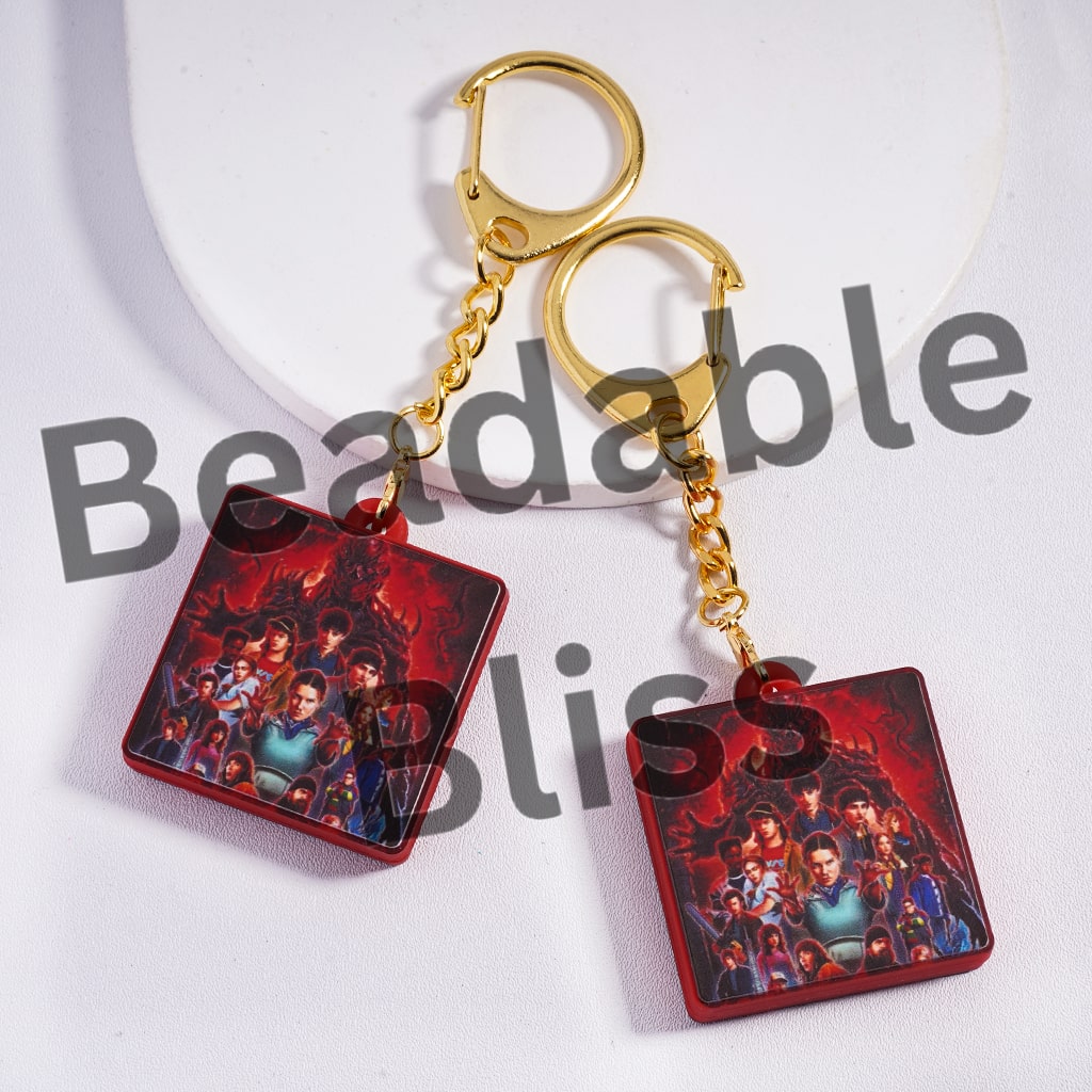 Pair of earrings with a gold chain and red square pendant featuring characters on a white background.