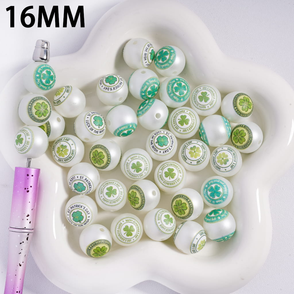 White beads with green shamrock designs in a white dish, with a pink pen on the side.