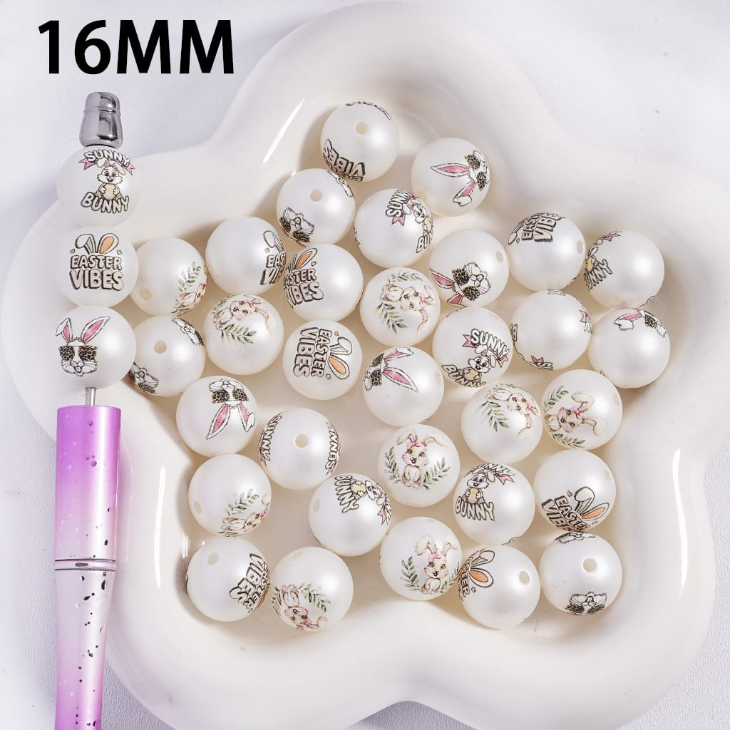 White beads with decorative engravings on a white plate, with a pink and silver tool next to them.
