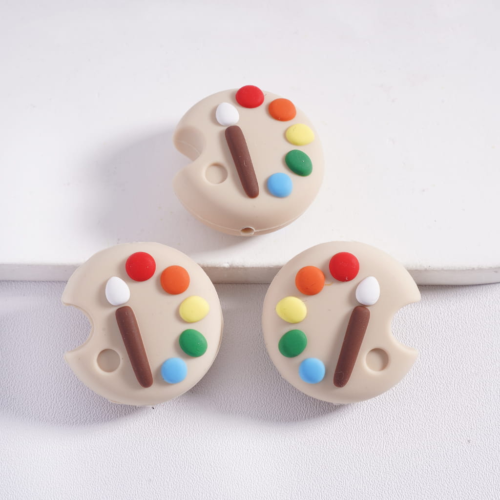 Three beige paint palette-shaped teething toys with colorful beads on a white background