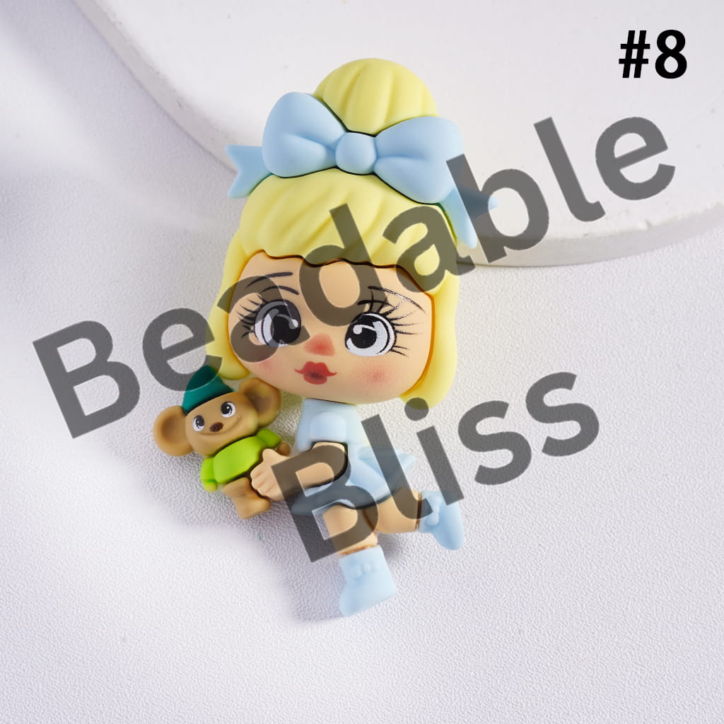 Toy figure of a girl with blonde hair and a blue bow, holding a teddy bear, on a white background