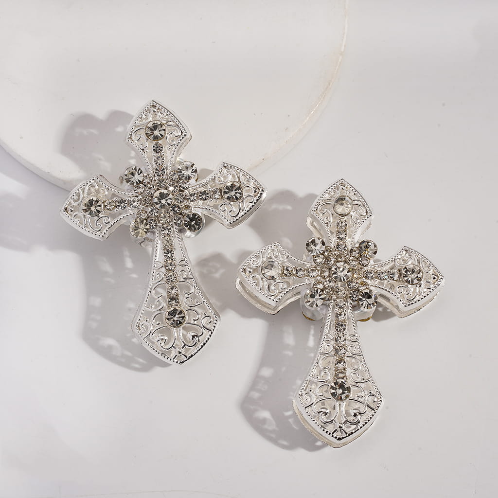 Silver cross-shaped earrings with gemstones on a light gray background