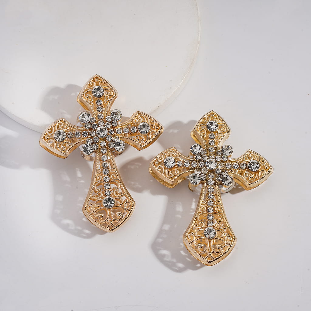 Gold cross earrings with intricate designs and clear stones on a light background