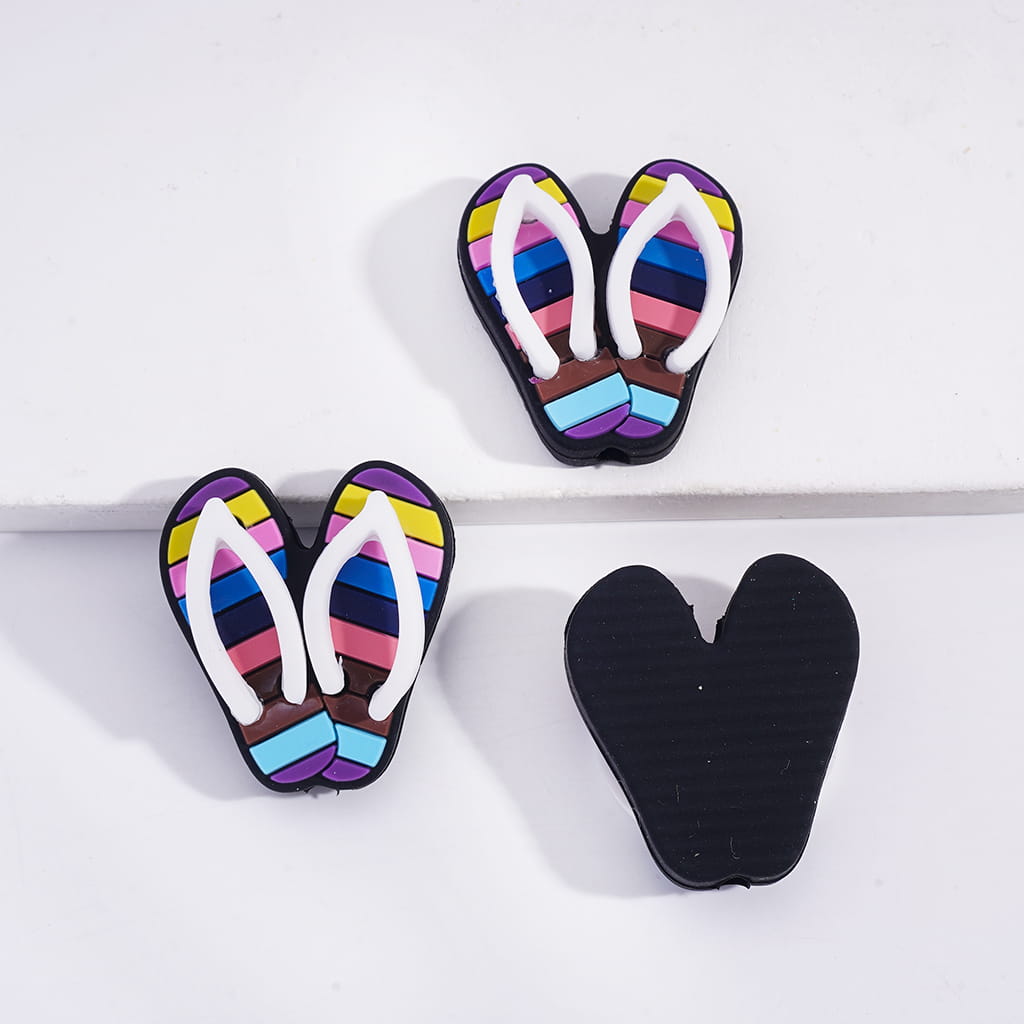 Colorful flip-flop earrings with a black heart-shaped object on a white background