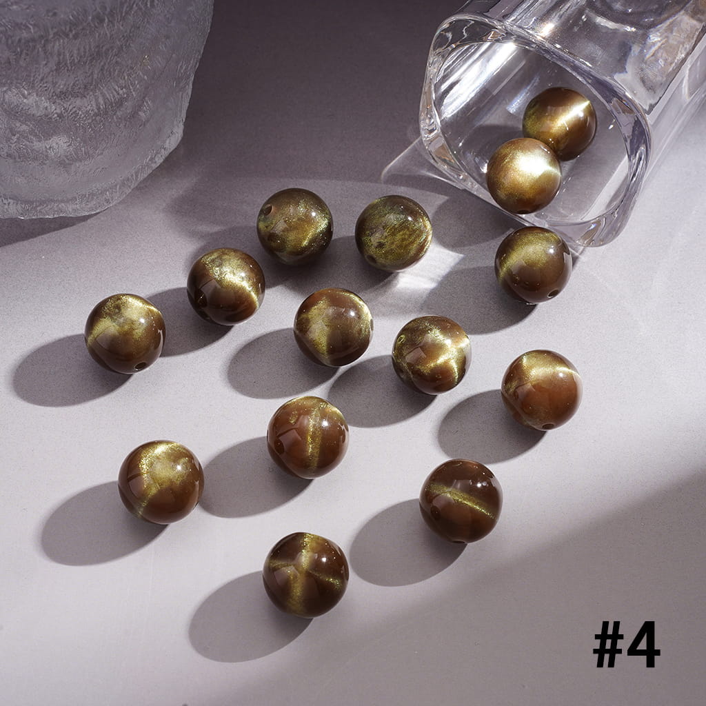 Gold-colored beads scattered on a light surface with a clear container partially visible.